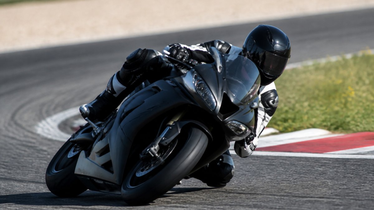 Sportmotor in volle snelheid door scherpe bocht op circuit, rijder in agressieve positie, zichtbare bandenslijtage en perfecte gewichtsverdeling, fel daglicht