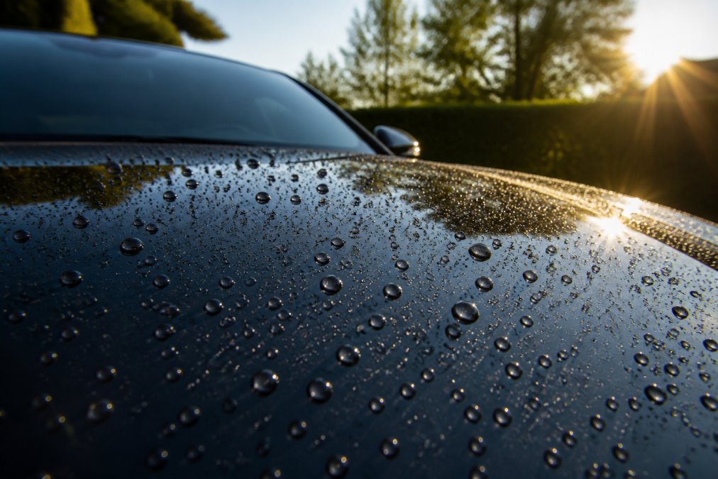 Close-up van water dat in perfecte parels afstuit op een glanzende autooppervlak met keramische coating, zonneschijn reflecterend in de diepe lak