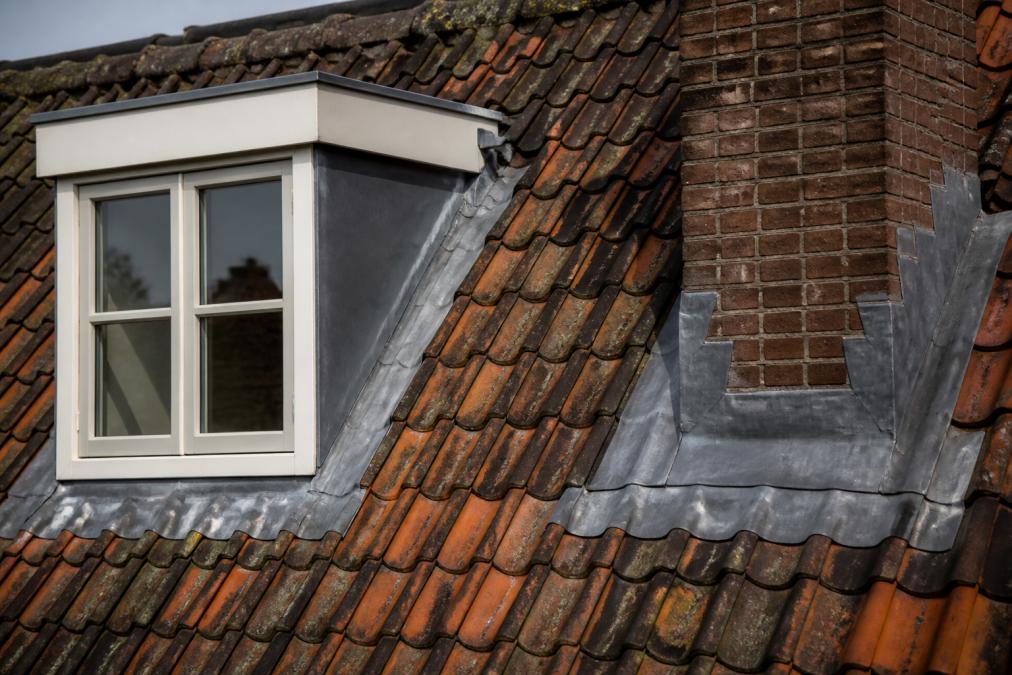 Detailopname van professioneel aangebrachte loodafsluitingen rond een dakkapel en schoorsteen op een historisch pand met originele pannendakbedekking