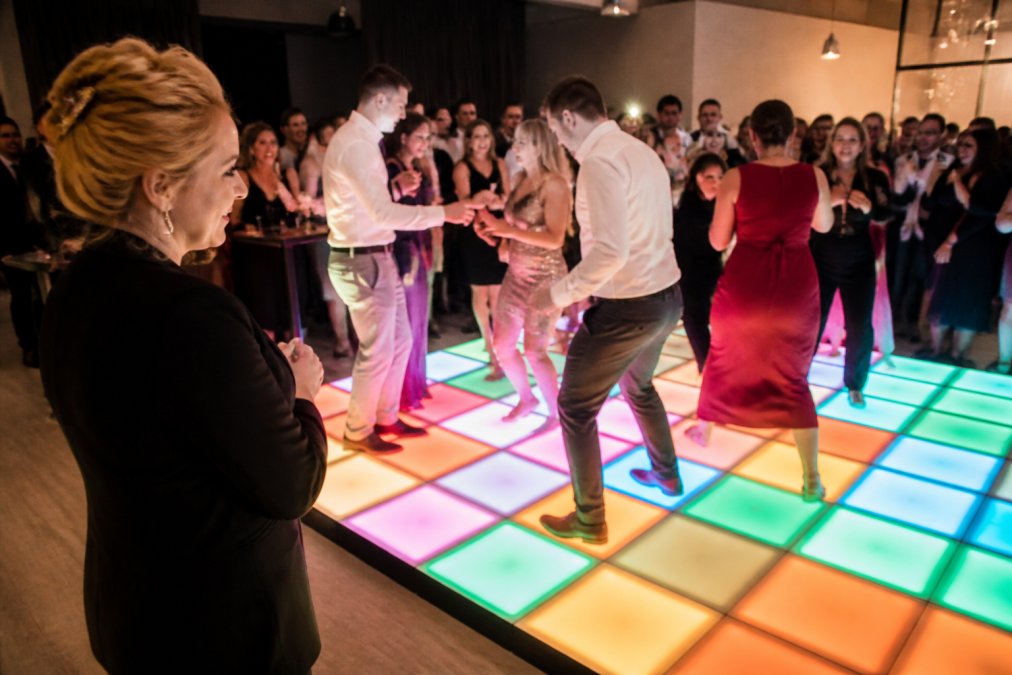 Een groep gasten dansend op een pixel LED-vloer met neon-gekleurde animaties, met Petra Keizer zichtbaar aan de zijkant die toekijkt