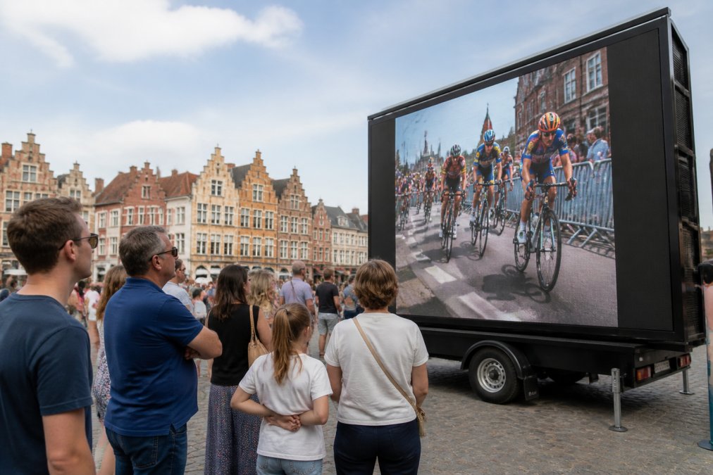Een mobiel LED scherm op een aanhangwagen tijdens een buiten evenement in een Belgische stad, bezoekers kijken geboeid naar het scherm bij helder daglicht