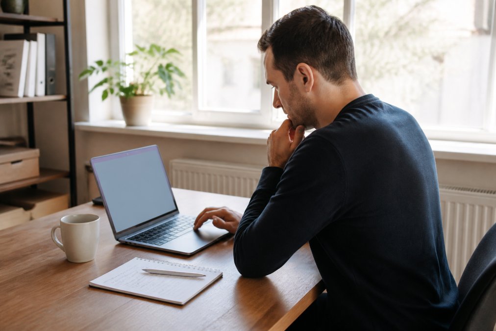 A focused entrepreneur sitting at a home office desk, laptop open with online incorporation forms on screen, a cup of coffee and a notebook with handwritten notes beside the keyboard, daylight coming through a window