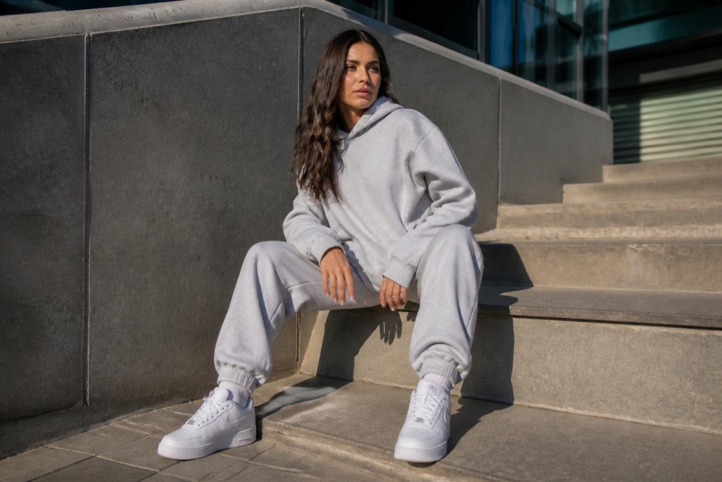 Vrouw in oversized hoodie en joggingbroek met sneakers, casual streetwear outfit buiten in zonlicht met ontspannen houding