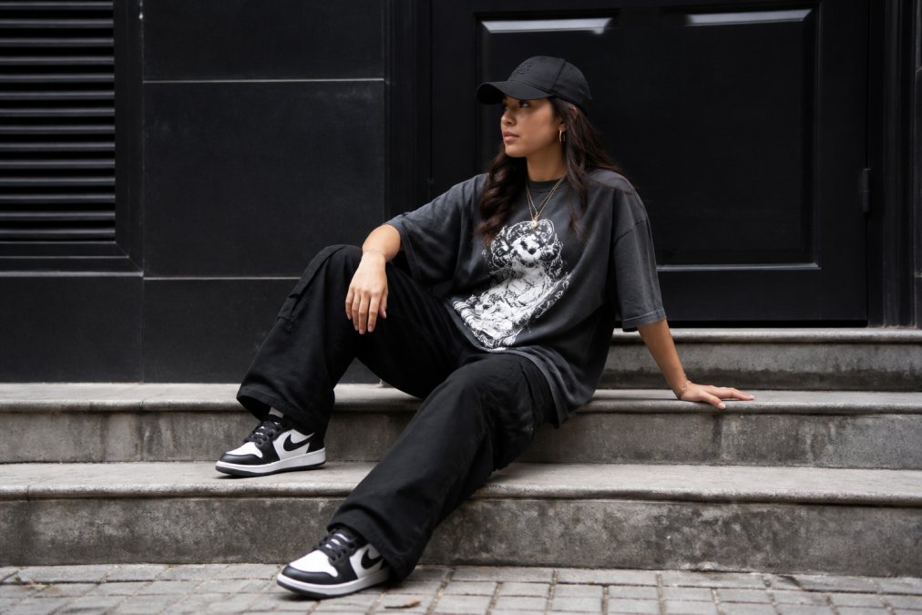 Vrouw in oversized t-shirt met print, gelayerd met cap en sneakers, complete streetwear outfit met accessoires buiten