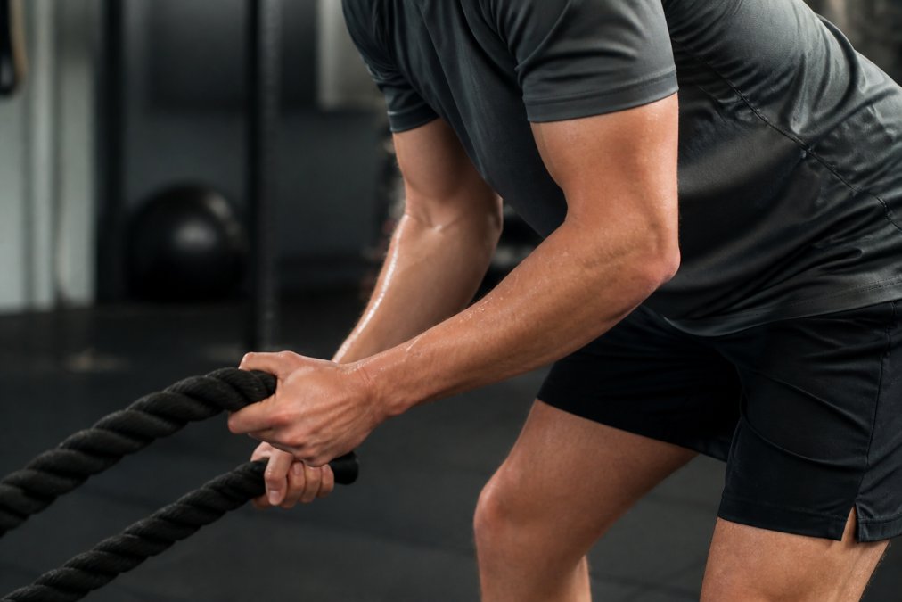 Close-up of athlete's hands and torso during intense cross-training workout, showcasing fitted athletic apparel with visible technical seams and moisture-wicking fabric construction, sweat visible on performance material