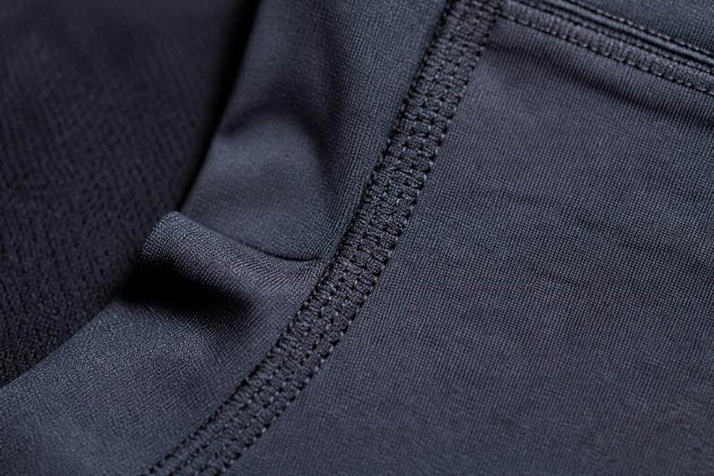 Close-up of high-quality seam construction and fabric weave detail on premium athletic apparel, showing reinforced stitching and dense fabric texture in natural lighting