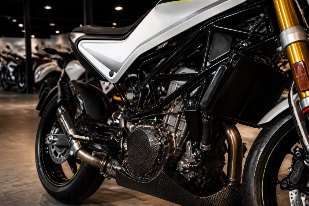 Close-up van een Husqvarna Factory Edition met carbon koppelingsdeksel en Öhlins vering, geparkeerd in een showroom met zachte spotverlichting die de details van het frame-ontwerp benadrukt