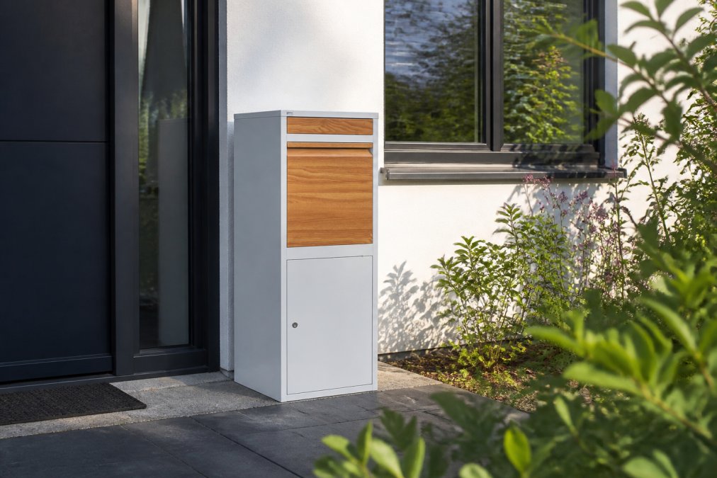 Moderne voorgevel met een elegante design pakketbrievenbus in gepoedercoat staal tussen groene planten bij natuurlijk