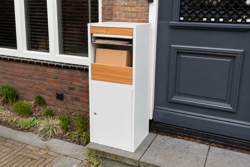 Close-up van een moderne, stijlvolle pakketbrievenbus aan de gevel van een woning, met post en pakketten zichtbaar in de opening, natuurlijk daglicht