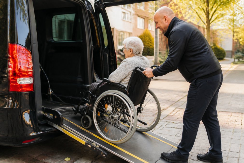 Vriendelijke chauffeur helpt een dame met deur tot deur rolstoelvervoer veilig de rolstoelbus in.