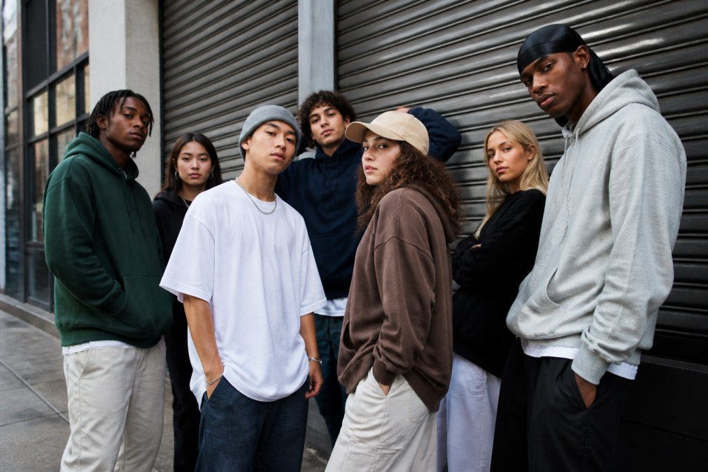 Diverse group of young people in modern streetwear outfits on the street, wearing hoodies, oversized T-shirts, and caps, posing confidently in an urban environment