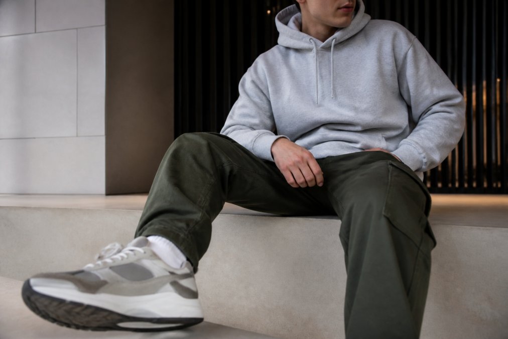 Close-up of someone wearing an HTT hoodie, styled with cargos and sneakers, sitting in a modern, minimalist setting