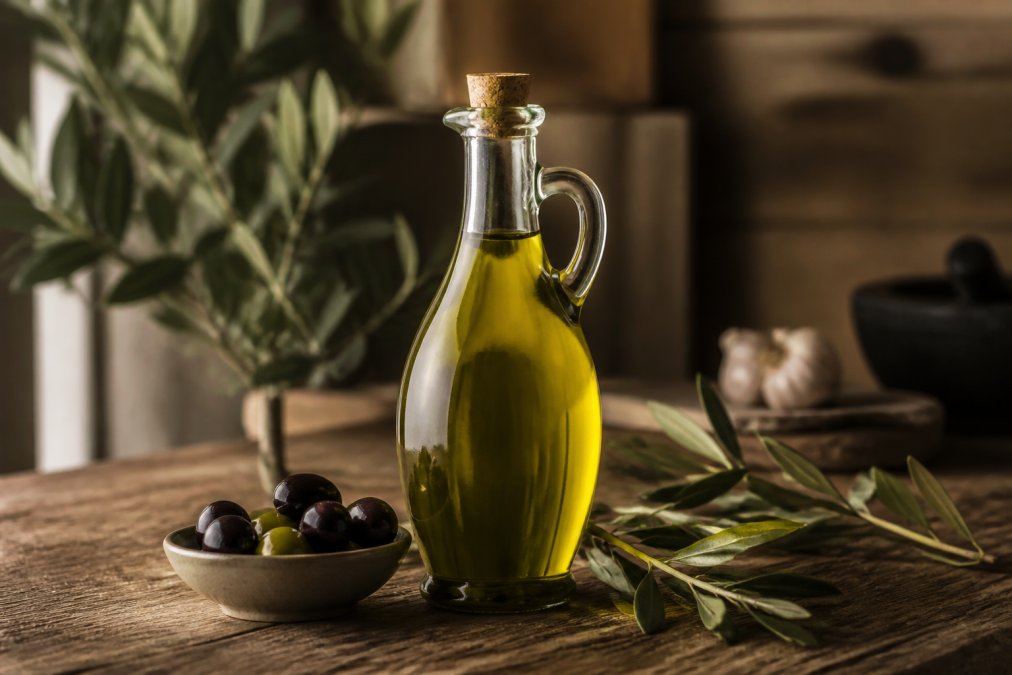 Een professionele chef in een keuken die premium olijfolie over een verse salade giet, met de fles duidelijk zichtbaar en natuurlijk licht dat de goudgroen kleur van de olie benadrukt
