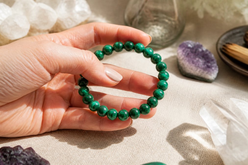 Close-up van een hand die een natuurlijke malachiet armband vasthoudt, met zachte natuurlijke lichtinval die de diepgroene kleur en glans van de stenen benadrukt
