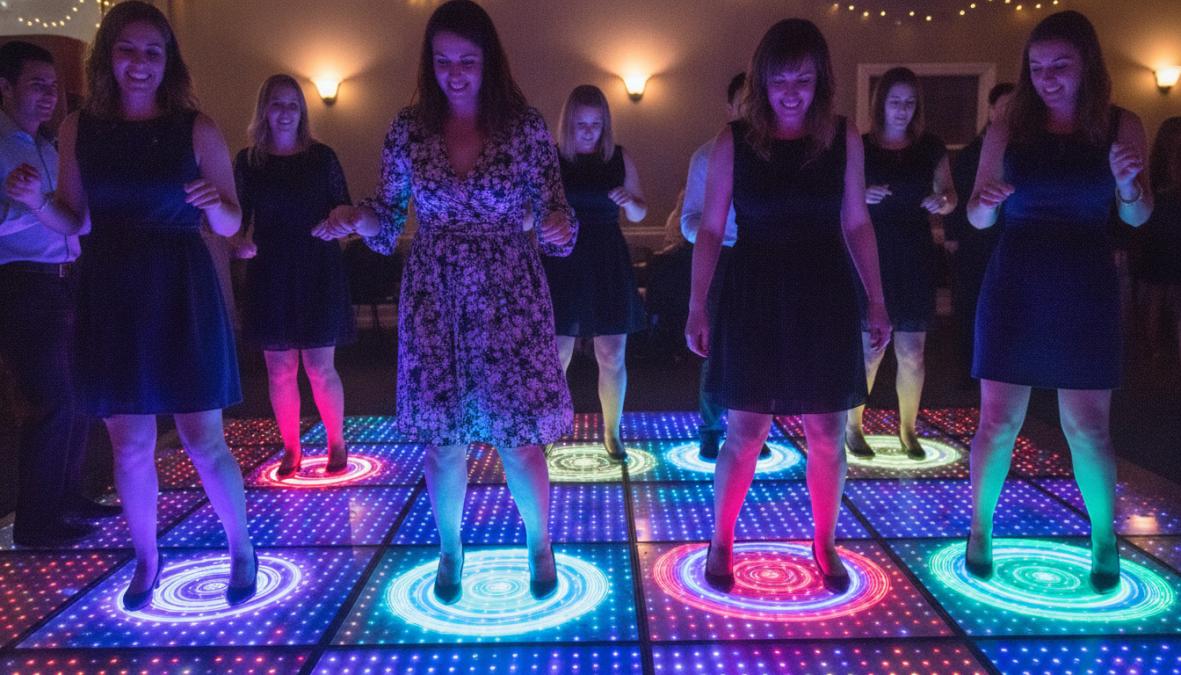 Groep feestgangers dansend op een verlichte LED dansvloer met levendige rode, blauwe en groene kleuren die onder hun voeten verschijnen, met zichtbare interactieve lichteffecten die meebewegen met hun bewegingen