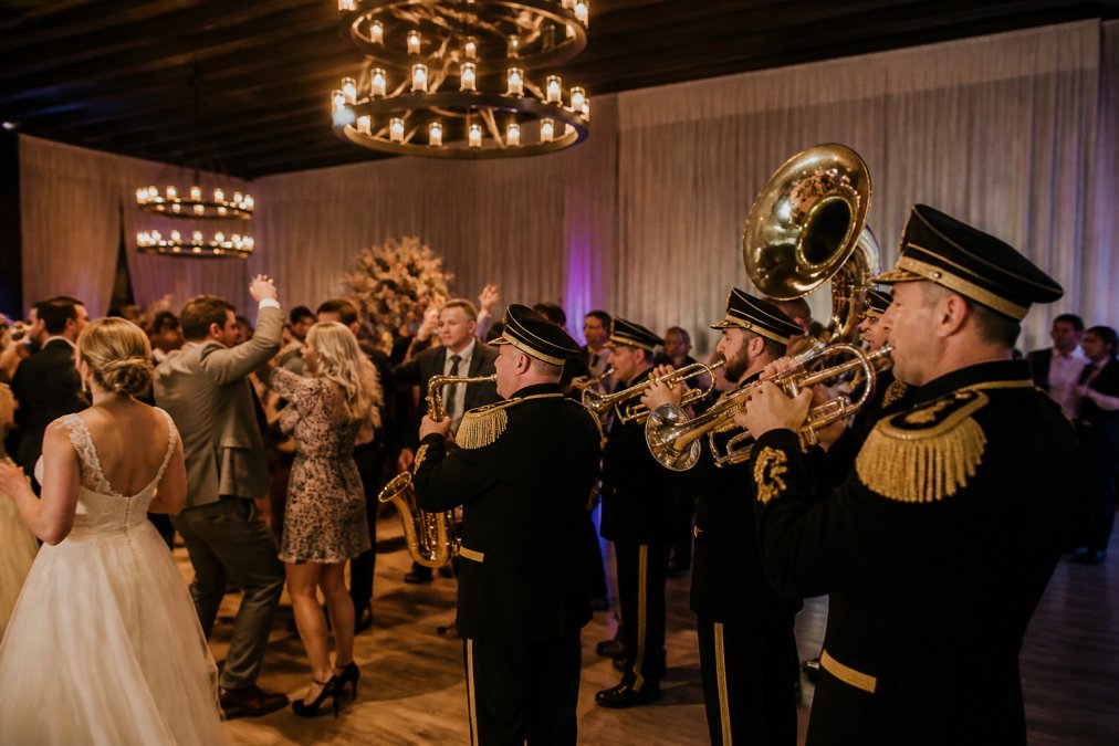 Professionele brassband in traditionele uniformen speelt live op een bruiloftsfeest in een stijlvolle zaal met gedimde verlichting, gasten dansen op de dansvloer