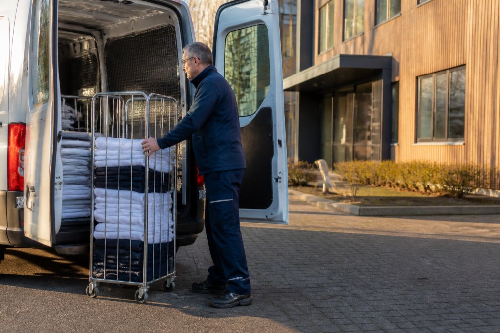 Medewerker laadt schone bedrijfskleding in een busje voor efficiënte kledingreiniging per kilo in Zuid-Limburg.