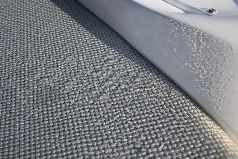 Close-up of woven vinyl flooring surface on a boat deck, showing the textured weave pattern with water droplets beading on the surface, natural sunlight, salt spray visible on adjacent gelcoat