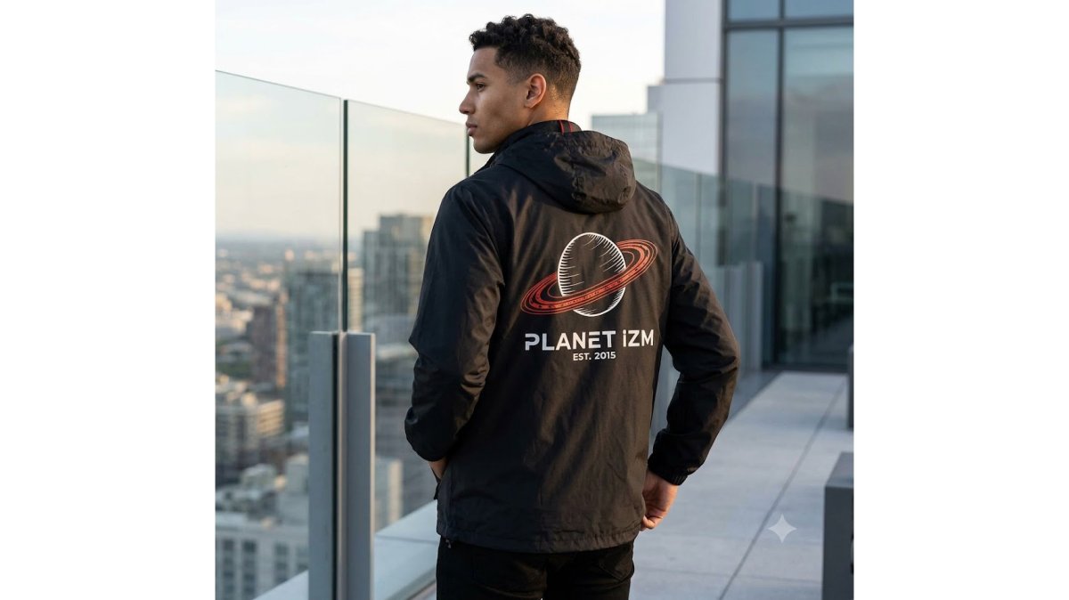 Person wearing a waterproof nylon anorak jacket over a fitted black long-sleeve shirt with visible structural seams and metal zipper hardware, standing in an urban setting with concrete and glass architecture in background, natural overcast daylight