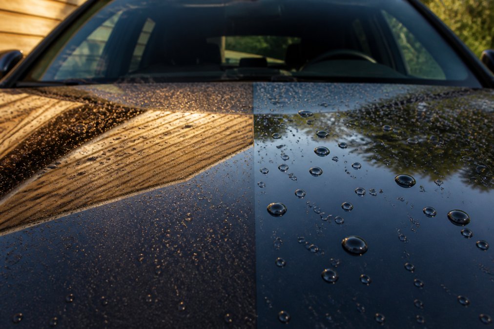 Close-up van twee autolakpanelen naast elkaar, één behandeld met carnauba wax met warme reflectie en één met synthetische sealant met scherpe glanzende reflectie, waterdruppels zichtbaar op beide oppervlakken