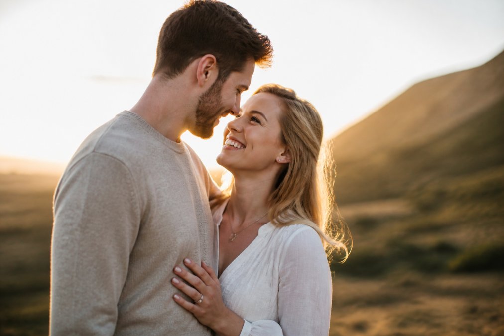 Bride and groom posing together for engagement photo outdoors, bride smiling naturally with soft golden-hour sunlight, aligners virtually invisible in professional photograph