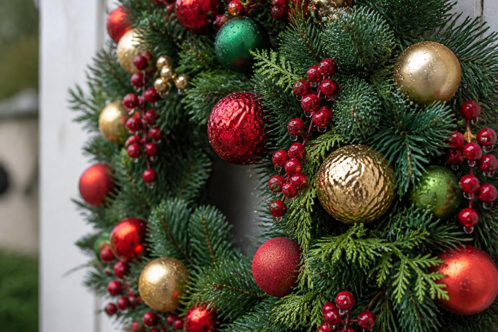 Close-up of weatherproof plastic holiday wreath with synthetic greenery and resin ornaments, water droplets visible on surface, showing proper material composition