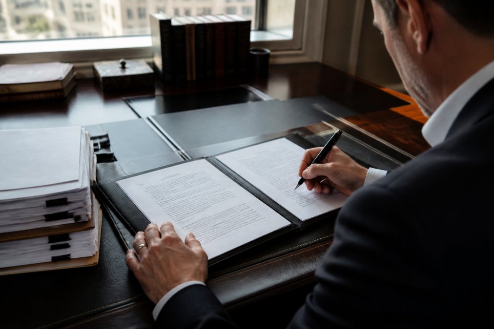 Professional reviewing webcast recording ownership documentation at a desk with contract papers, laptop displaying copyright terms, and pen ready to sign
