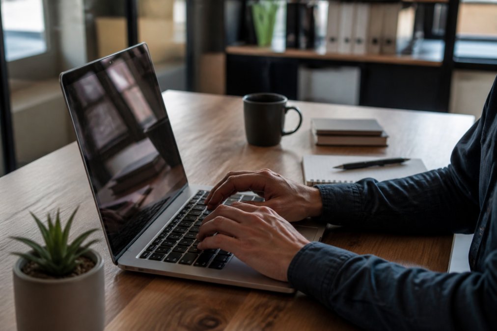 Person's hands on a laptop keyboard with website builder interface visible on screen in a modern workspace with natural lighting