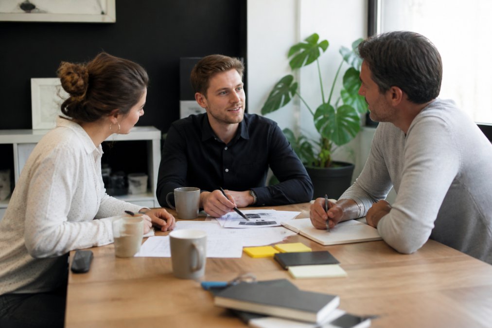 Team van webdesigners en ondernemer in gesprek aan bureau met laptop, notities en koffie, besprekend website aanpassingen