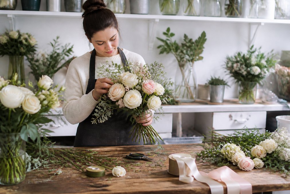Florist arranging a bouquet of white and blush roses for professional wedding floral design in a bright studio