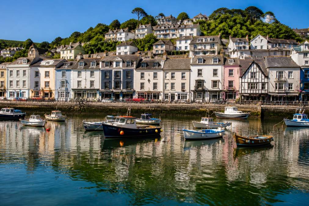 Picturesque coastal harbour town with colourful waterfront buildings, boats moored in the estuary, and historic architecture reflected in calm water