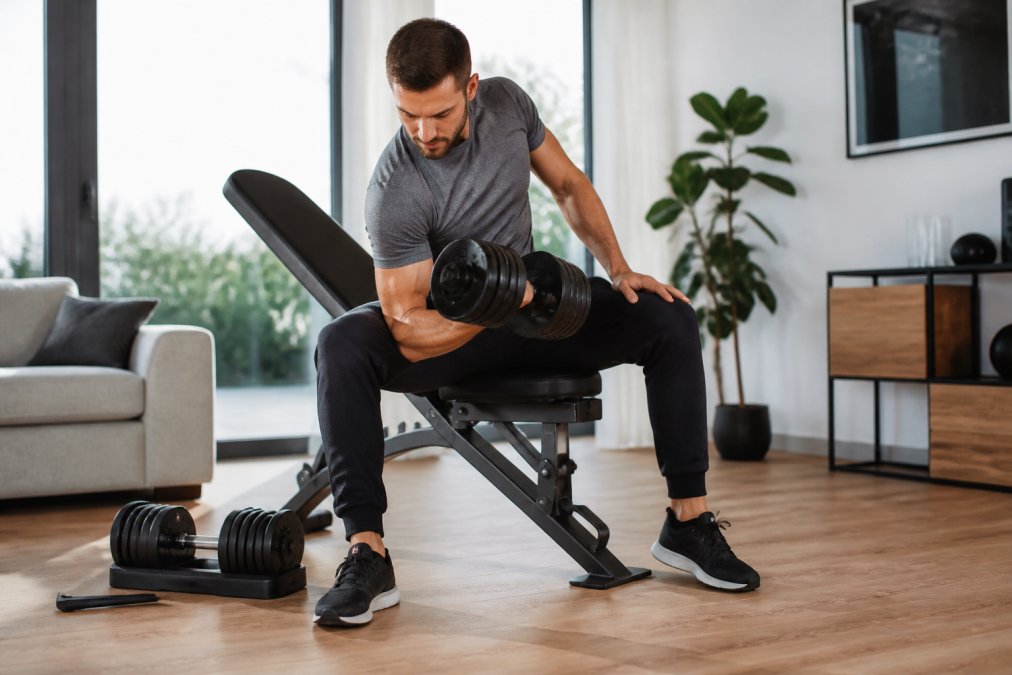 Ein Mann trainiert mit verstellbaren Kurzhanteln auf einer modernen Hantelbank, wenn Sie sich fragen, welche fitnessgeräte