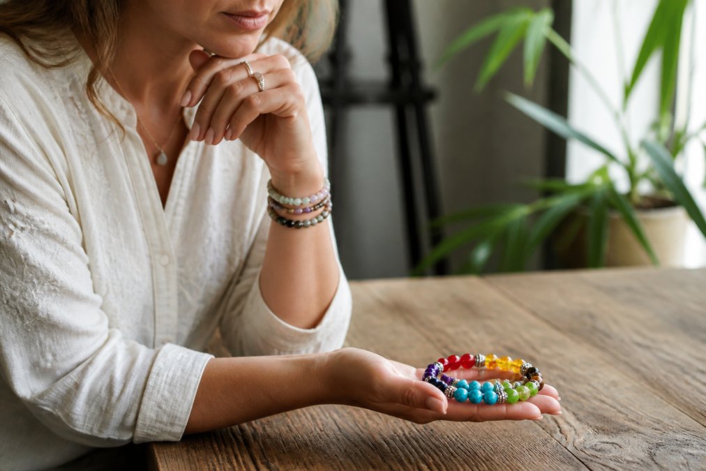 Close-up van vrouwenhanden die meerdere kleurrijke edelsteenarmbandjes vasthouden op een houten ondergrond, met zacht natuurlijk licht, de vrouw kijkt bedachtzaam en kalm