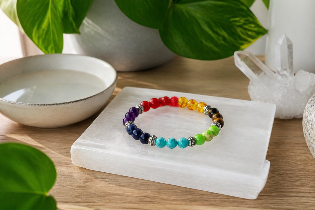 Een edelsteenarmband rustend op een witte selenietplaat naast een kleine kom water en een groene plant, in een serene, zacht verlichte thuisomgeving