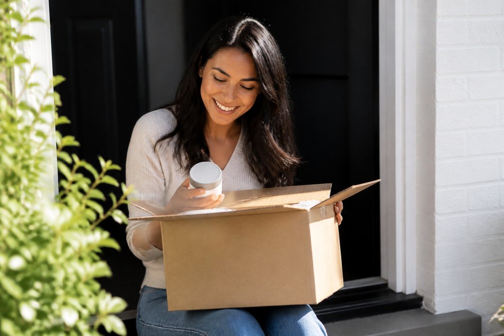 Person receiving a wellness product package at their doorstep in natural daylight, opening the box with a satisfied expression to check contents