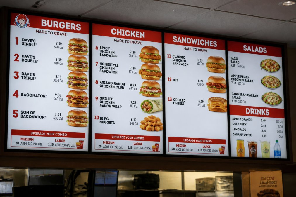 Close-up of a Wendy's menu board displaying burger, chicken, and sandwich categories with clear pricing visible under bright restaurant lighting