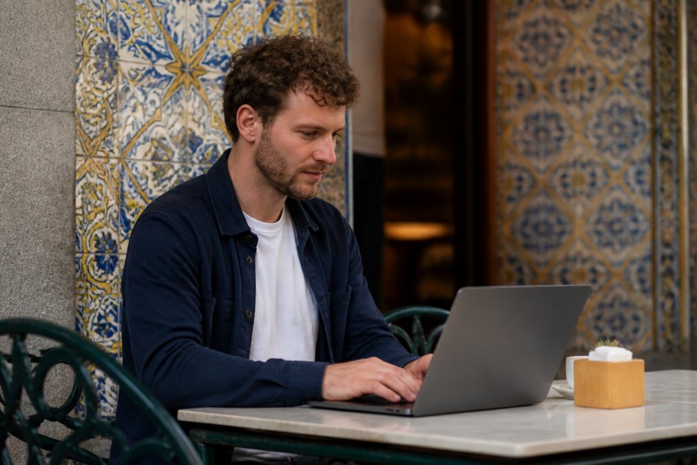 Digitale nomade werkend aan een laptop in een gezellig café met traditionele Portugese tegels, blauwe en gele azulejos, en lokale sfeer op de achtergrond