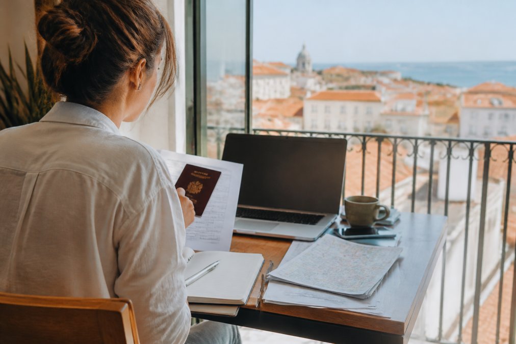 Persoon die aan een bureau zit met een laptop, paspoort, en reisdocumenten voor voorbereiding op verblijf in Portugal