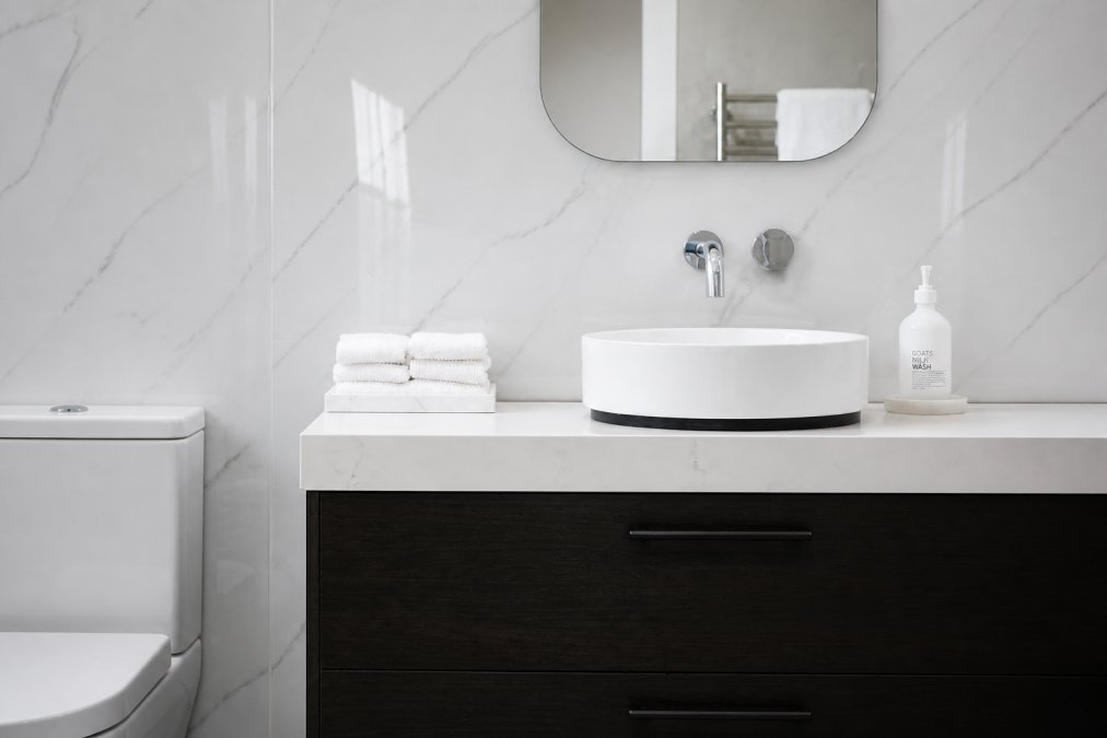 Modern bathroom with gleaming waterproof wall panels in white marble-effect finish, showing seamless joints and clean reflective surface under bright bathroom lighting