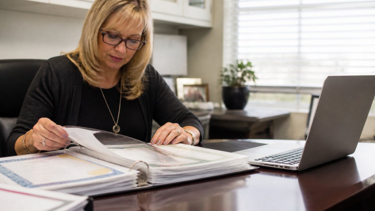 Administrator reviewing staff certificates for assisted living training records in a bright office.