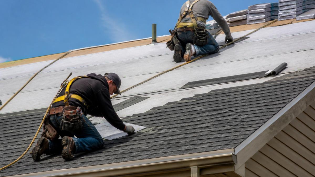 Roofing crew wearing safety harnesses installing underlayment and flashing during a new roof installation.