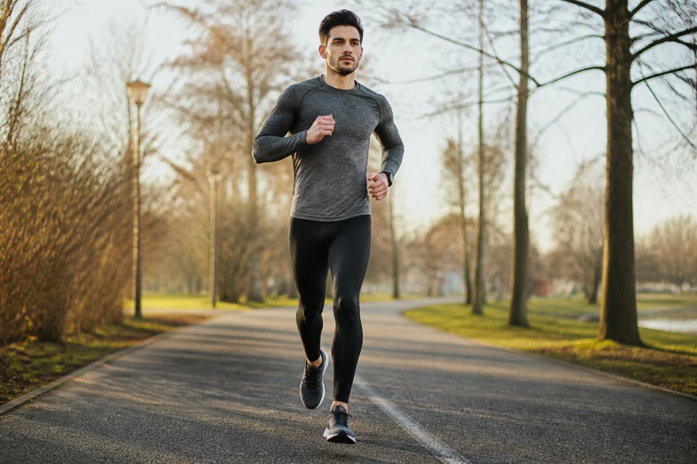 Runner in black compression gear sprinting along a paved park path at dawn