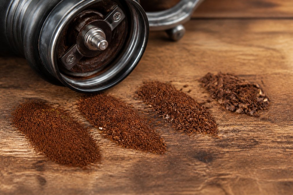 Close-up of a burr grinder with freshly ground coffee, showing different grind textures from fine to coarse on a wooden surface