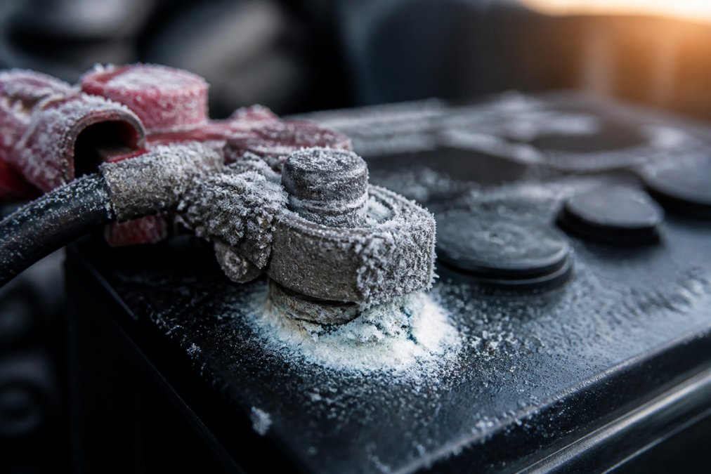 Close-up of frost and ice crystals forming on a car battery terminal with visible corrosion and white crystalline buildup in early morning winter light