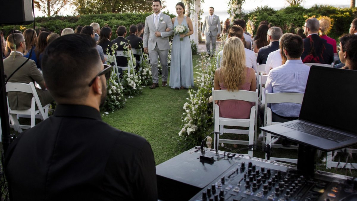 Wedding guest watching the bridal party walk down the aisle as a wedding DJ manages the ceremony music cues