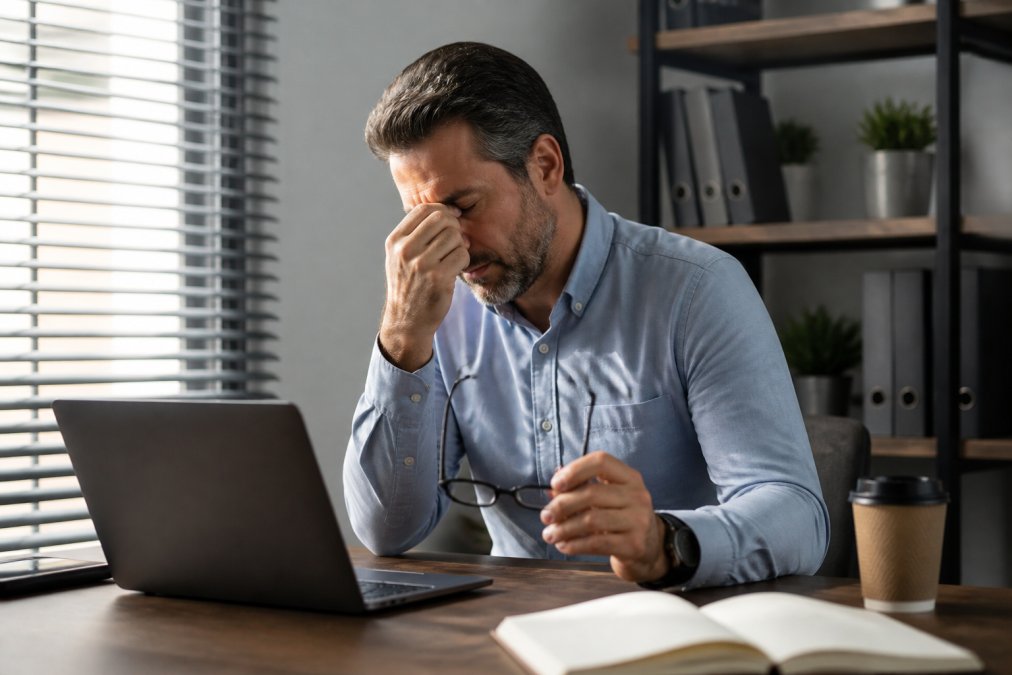 Man in his 40s rubbing tired eyes at a desk, struggling with low cellular energy during the workday.