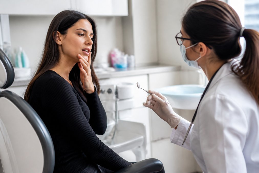 Patient seated in a dental chair speaking with a dentist during examination in a calm, modern clinical environment with soft overhead overhead lighting