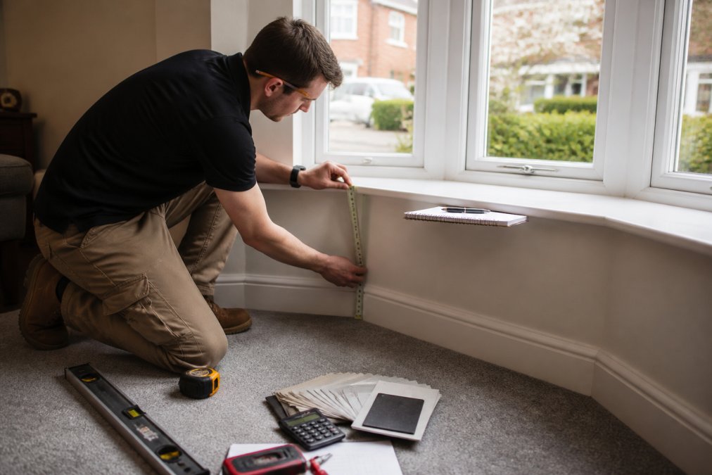 Person using a metal tape measure on a bay window to ensure they do not measure windows wrong while recording dimensions.