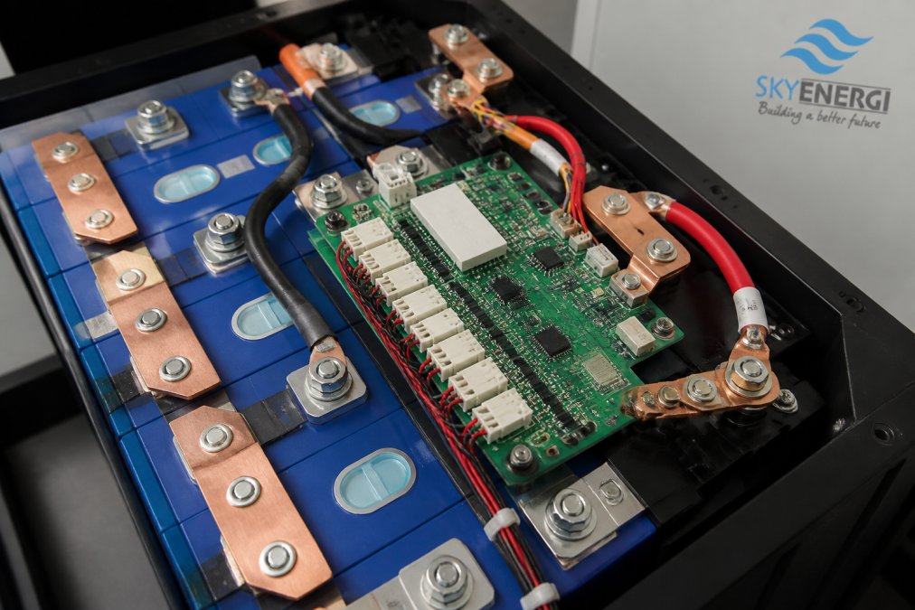 Close-up of a lithium battery pack interior showing individual cells connected to an electronic circuit board with monitoring sensors and copper terminals