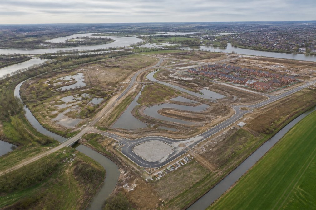 Aerial view of a residential development site with visible water management features, drainage channels, and surrounding topography during a rainfall event